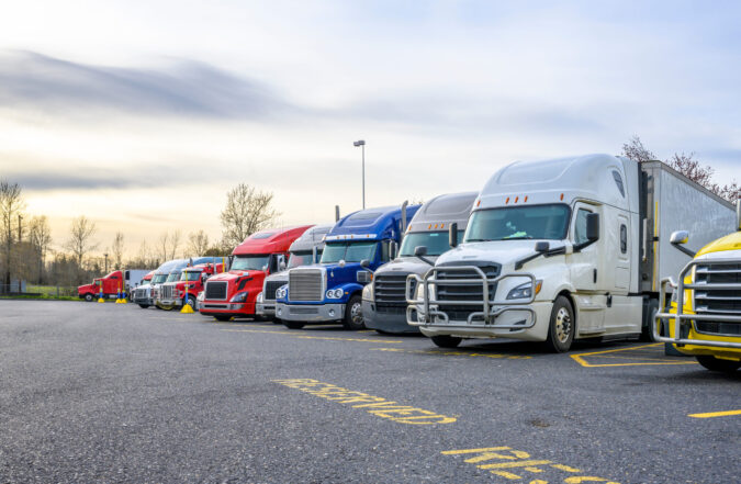 Different big rigs semi trucks with semi trailers standing in ro